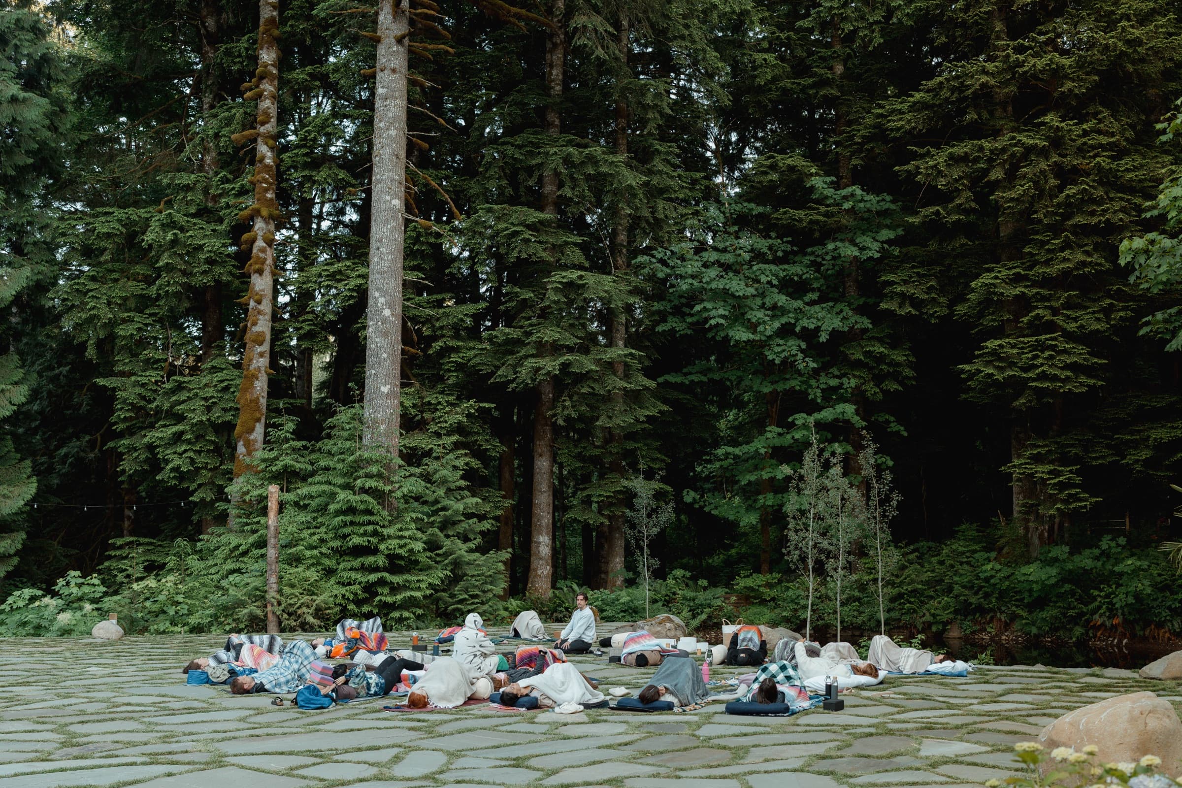 A group resting on blankets on the flagstone patio under tall firs at Highland Farms