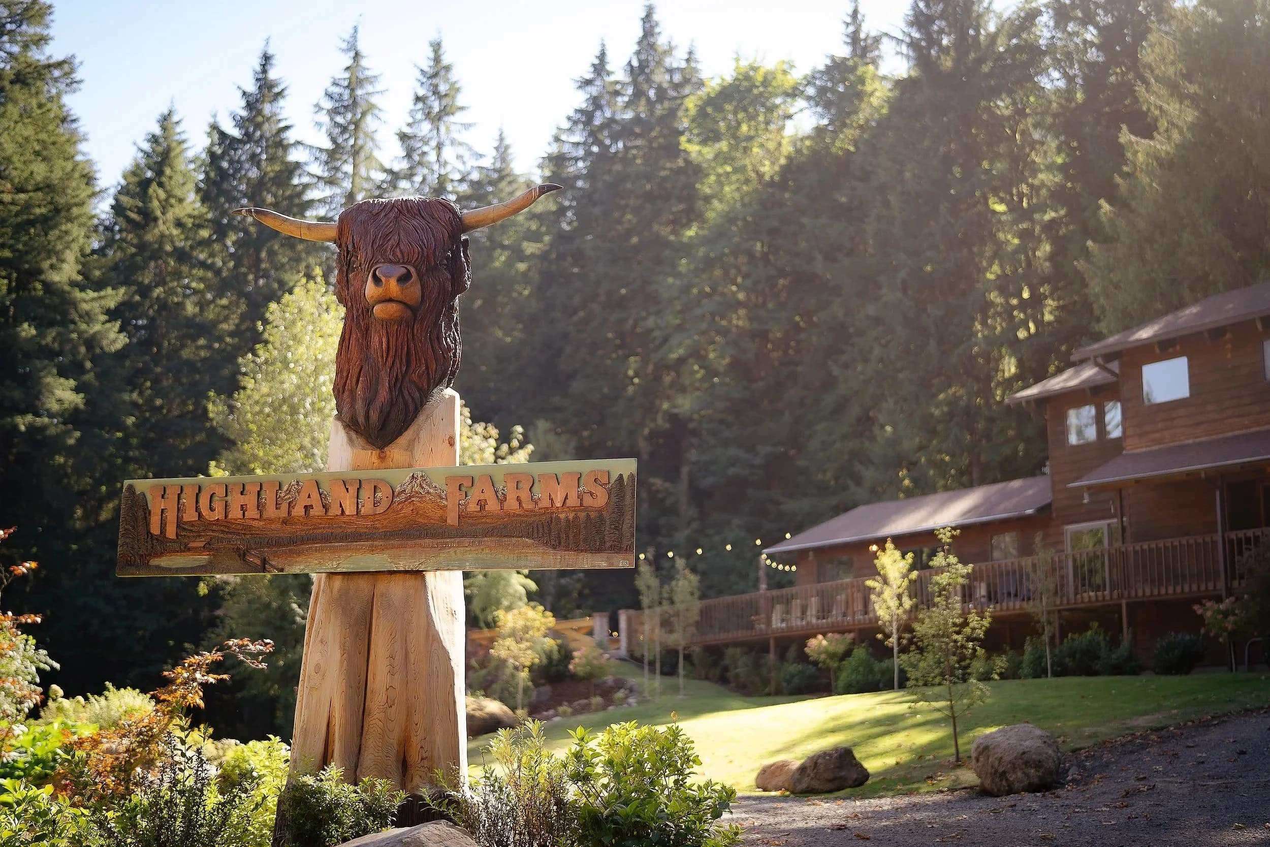 The carved wooden Highland cow holding the Highland Farms sign, the Lodge behind