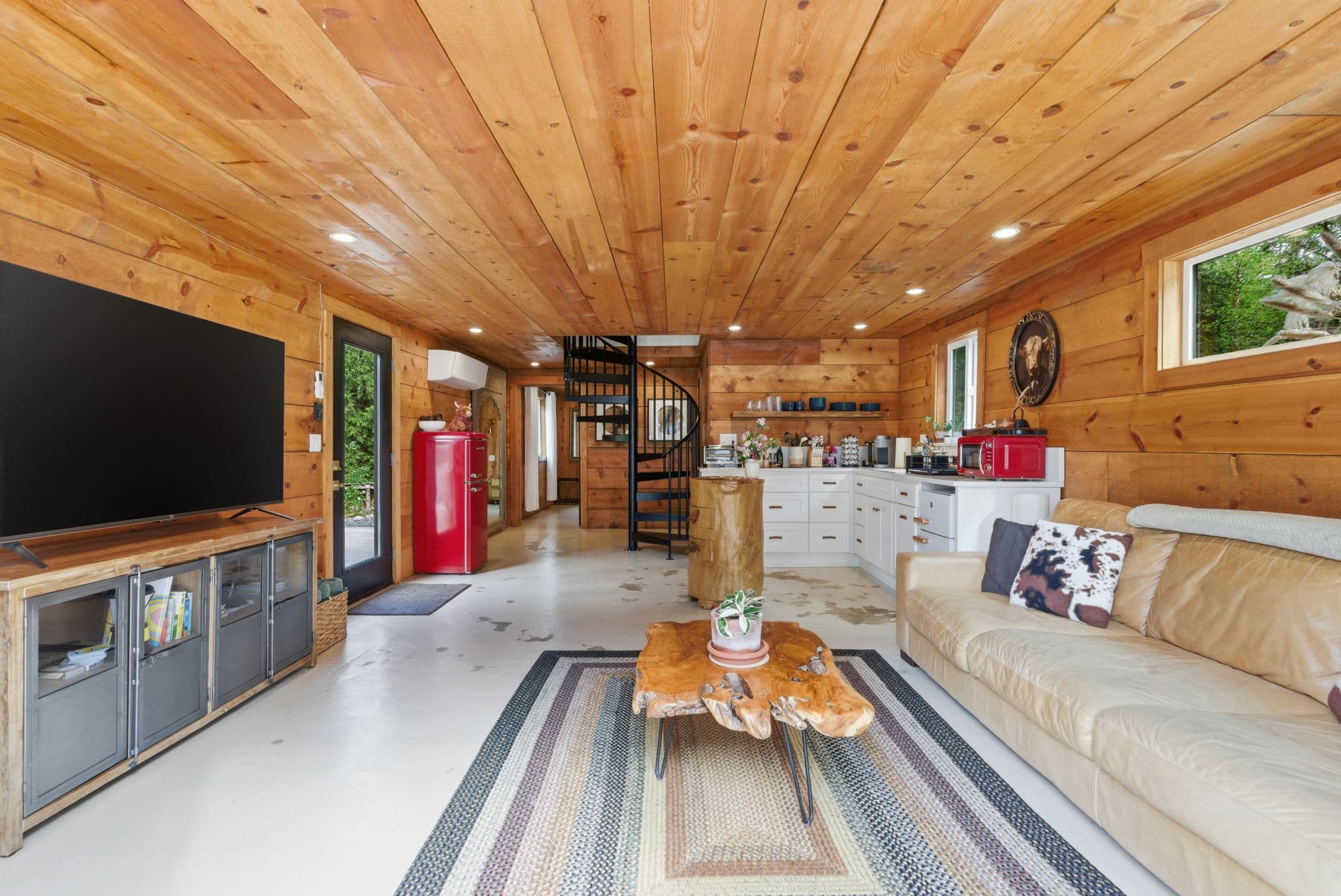 Cottage living room with spiral staircase, retro red fridge, and cedar-plank ceiling