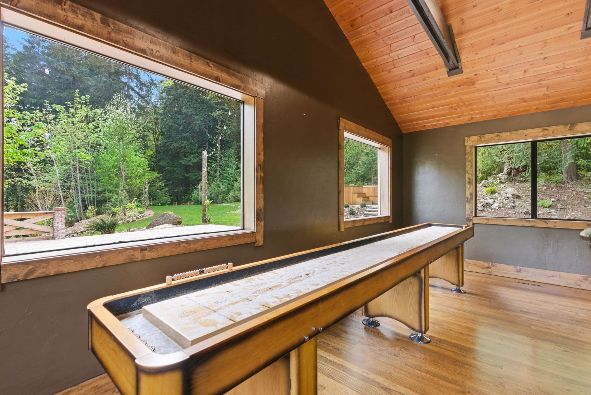 Game room with a full-length shuffleboard table and floor-to-ceiling forest windows