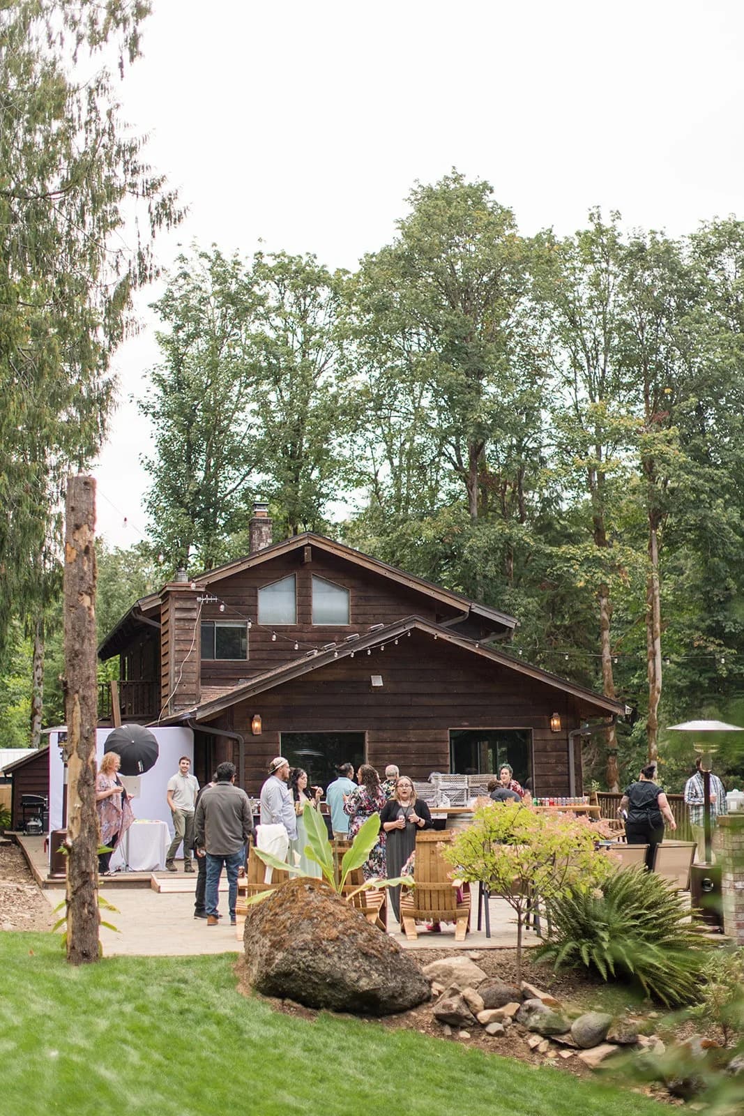 Guests gather on the patio in front of a dark-timbered building among tall trees