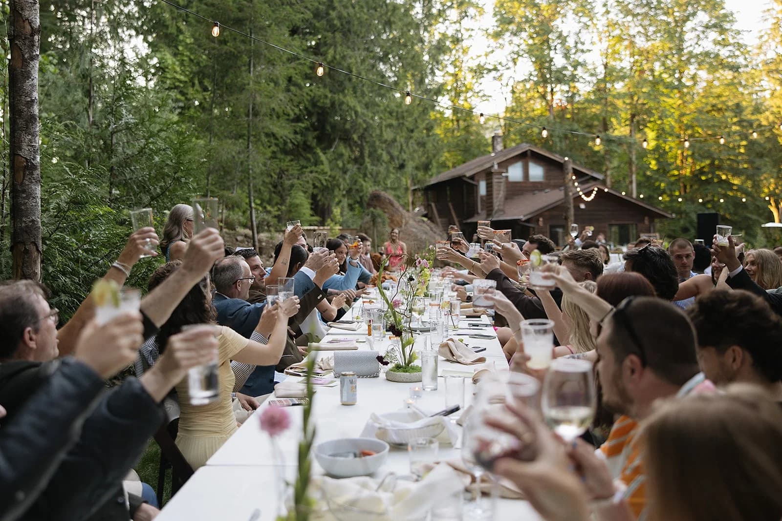 Guests raise their glasses along one long table under the trees